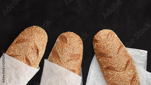three breads with sesame seeds wrapped in paper on black background top view