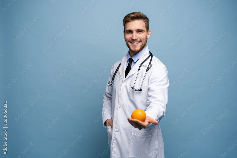 Happy young doctor offering you orange isolated over light blue. Happy young doctor offering you orange isolated over light blue.