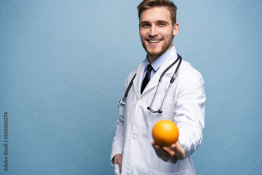 Happy young doctor offering you orange isolated over light blue. Happy young doctor offering you orange isolated over light blue.