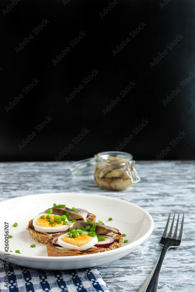 smorrebrod sandwiches with herring boiling egg chopped green onions  on white plate  fork napkin on wooden table vertical orientation