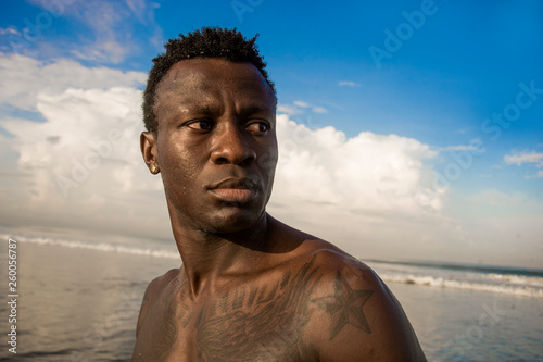 portrait of young attractive and fit black afro American man with strong muscular body posing cool model attitude on the beach isolated on Summer blue sky