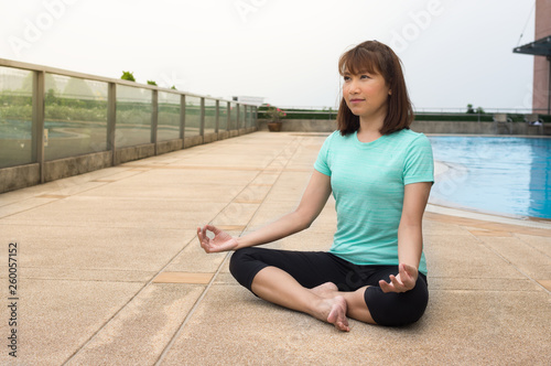Female doing Yoga meditation near swimming pool.