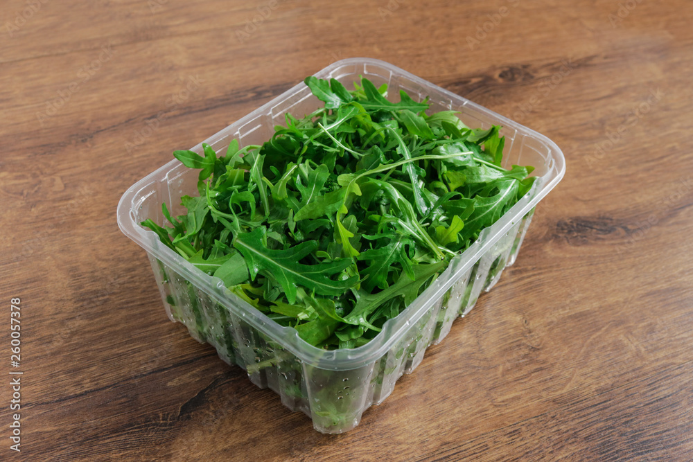 organic arugula salad in plastic container on wooden background organic arugula salad in plastic container on wooden background