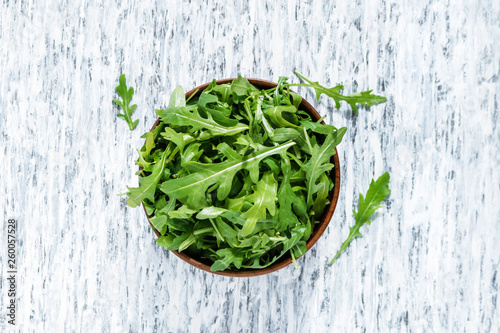 fresh arugula leaves in wooden bowl on white rustic background top view