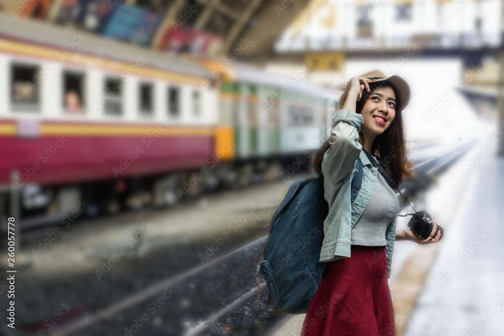 Smiling young Asian backpacker female standing at train station. Travel lifestyle concept.