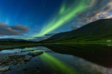 aurora borealis in night sky cut  mountains, reflected in  water.