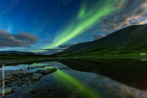 aurora borealis in night sky cut mountains, reflected in water.