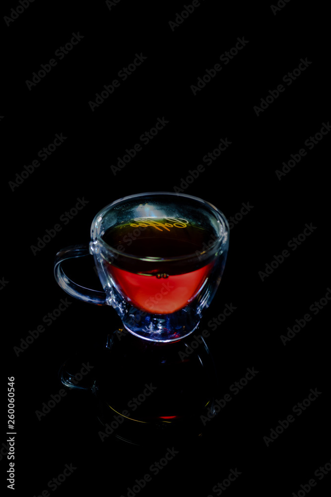 Tea in a transparent mug on a black background with reflection