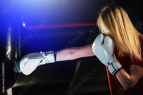 Woman hits the boxing heavy bag in the gym. Hard mixed martial arts training