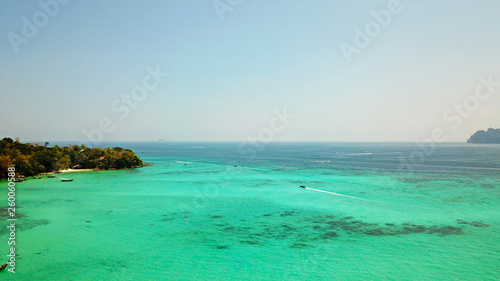 Blue clear water with boats. Green tropical island Phi Phi  palm trees grow. Shooting from a drone from the air. Beautiful seascape. Turquoise color of the water  you can see the bottom and corals.