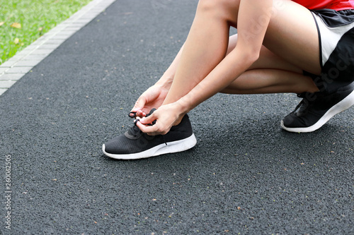 Healthy Asian woman tying shoelaces on running shoes on the street. Fitness and workout wellness concept.