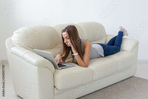Technologies, relax and freelance concept - pretty young woman lying on sofa and working on laptop