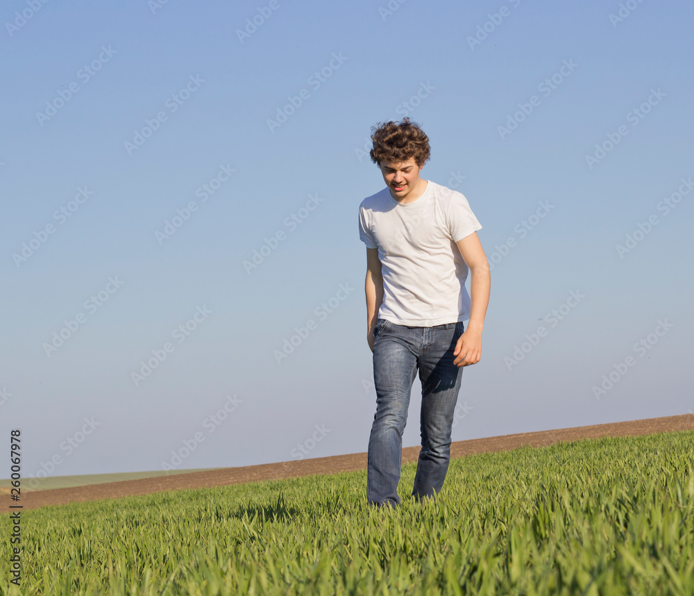 boy teenager walking on a field covered with green shoots of wheat