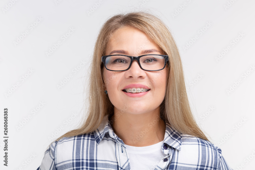 Teeth health, dentistry and bite correction - Happy smiling woman in glasses with braces on white background Teeth health, dentistry and bite correction - Happy smiling woman in glasses with braces on white background