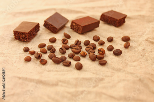 Chocolate cubes with coffee beans on a linen texture background.