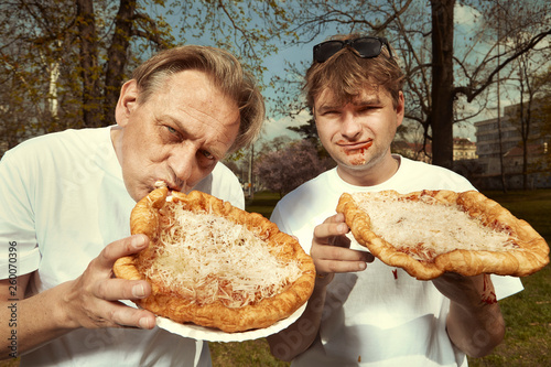 Men in street park eating langos with garlic  ketchup and cheese
