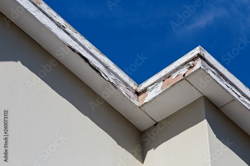 Roof repair and maintenance concept image consisting of old rotting fascia boards and a blue sky background. 