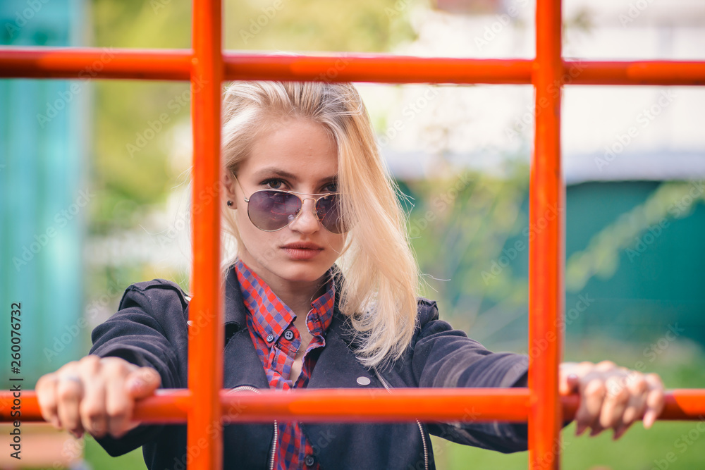 Cool girl in sunglasses looking through the net on the Playground in the Park for a walk. Cool girl in sunglasses looking through the net on the Playground in the Park for a walk.