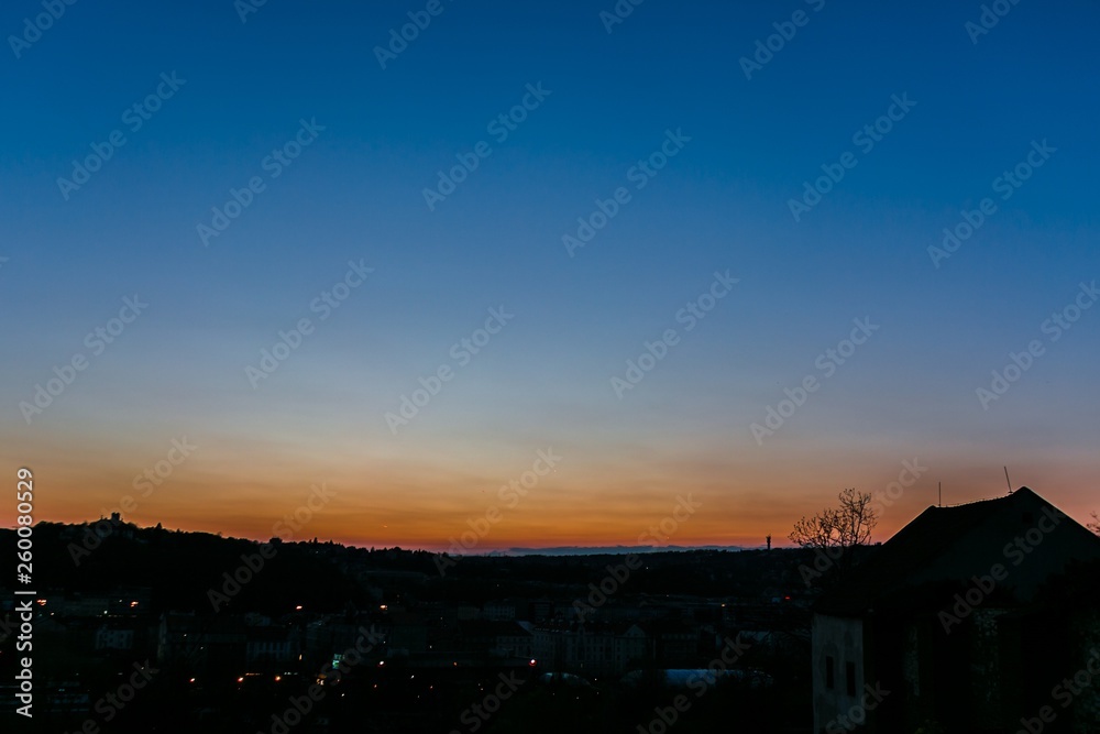 Blue sunset sky with orange and yellow colors above dark horizon, night urban landscape, copy space