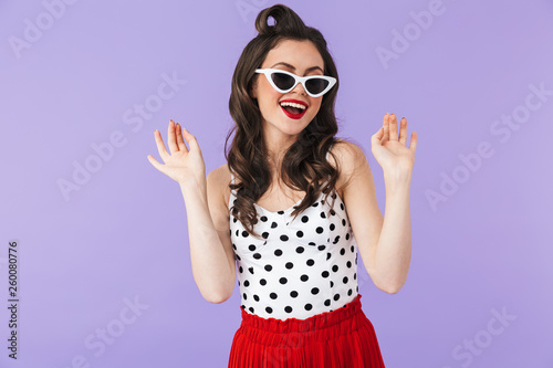 Portrait of stylish pin-up woman 20s in vintage polka dot dress and retro sunglasses smiling at camera