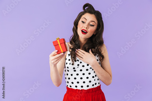 Portrait of coquette pin-up woman 20s in vintage polka dot dress smiling while holding red present box