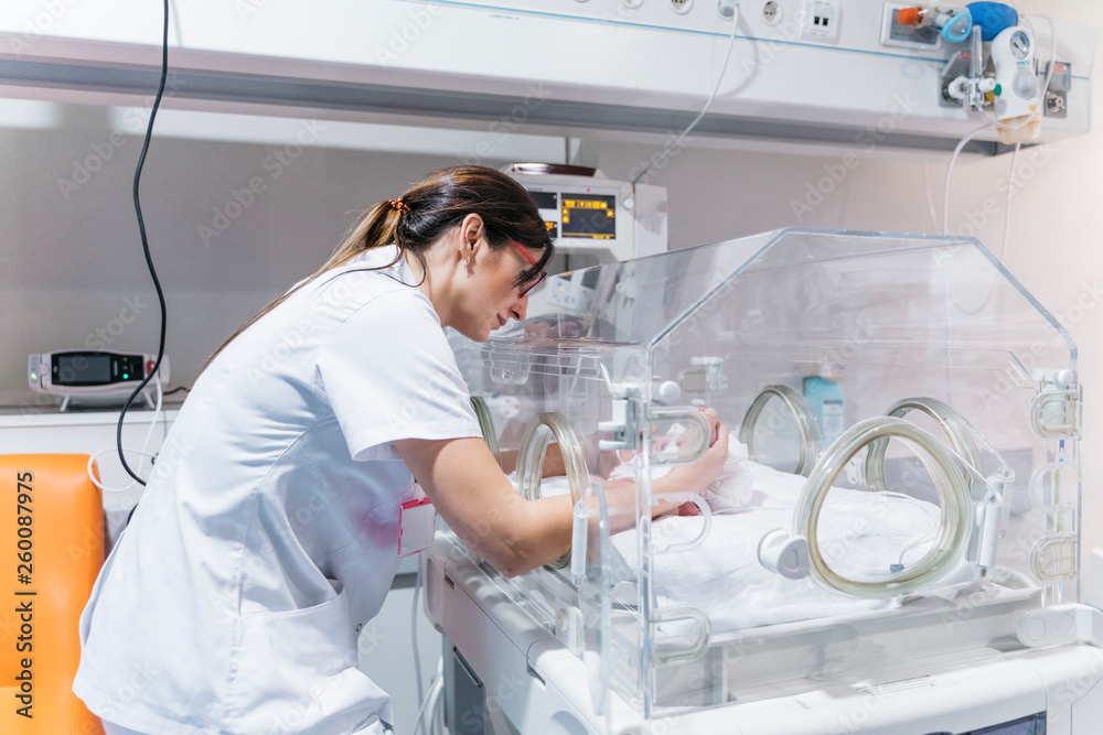 Female doctor examining newborn baby in incubator - obrazy, fototapety, plakaty 