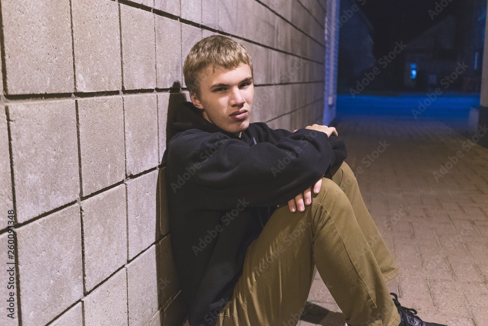 Sad teen sitting in an alleyway all alone at night.