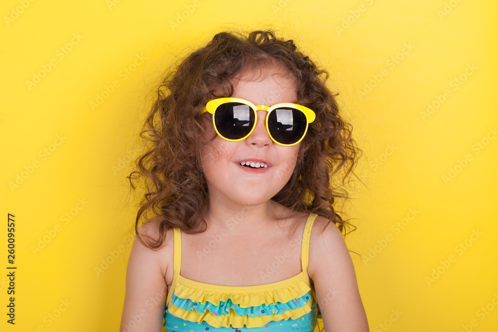 Little girl in a bathing suit and sunglasses on a yellow background Little girl in a bathing suit and sunglasses on a yellow background