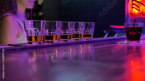 nightclub on the bar counter glasses with alcohol in the background the girl barman dancing in a white T-shirt.