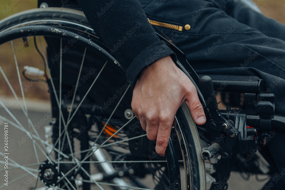 Close-up of male hand on wheel of wheelchair during walk in park Close-up of male hand on wheel of wheelchair during walk in park