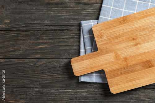 Cutting board with kitchen towel on wooden background, space for text