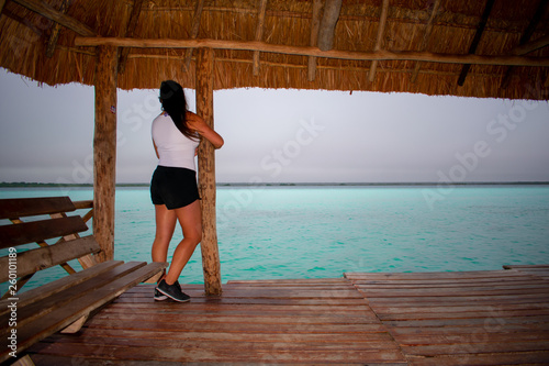 Back view of Young woman standing on wooden bridge on Bacalar Lake, Clear turquoise water in Mexico. 