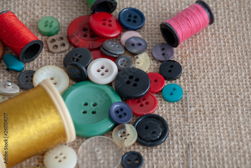 Top view of defocused golden thread spool and focused buttons on burlap cloth