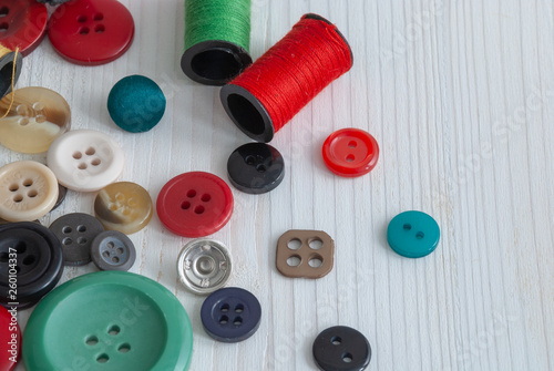 Top view of spools of thread and buttons on white wooden background