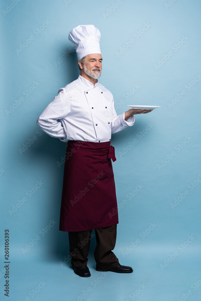 Full length of a professional chef holding an empty plate isolated on light blue. Full length of a professional chef holding an empty plate isolated on light blue.