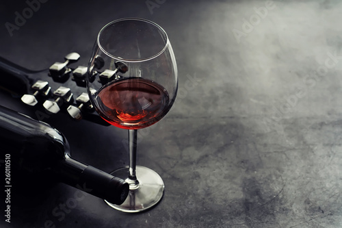 Guitar and high glass with red wine on a stone background.