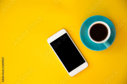 A blue cup with coffee and a mobile phone stands on a yellow background. Morning breakfast, business.