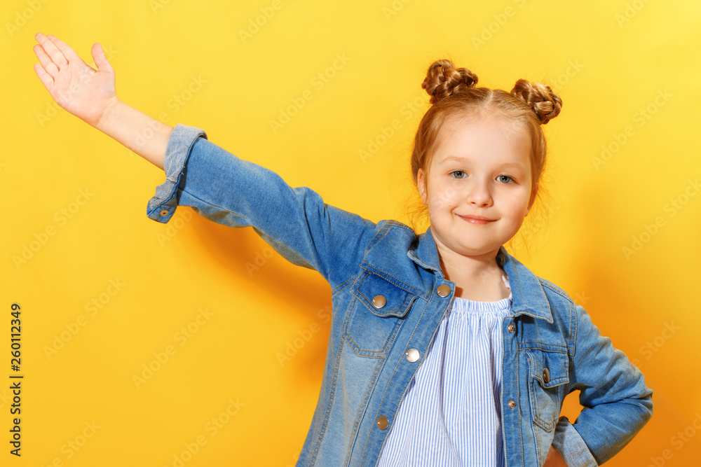 Closeup portrait of a cute attractive little girl on yellow background. The child points his hand to the top and looks into the camera. Closeup portrait of a cute attractive little girl on yellow background. The child points his hand to the top and looks into the camera.