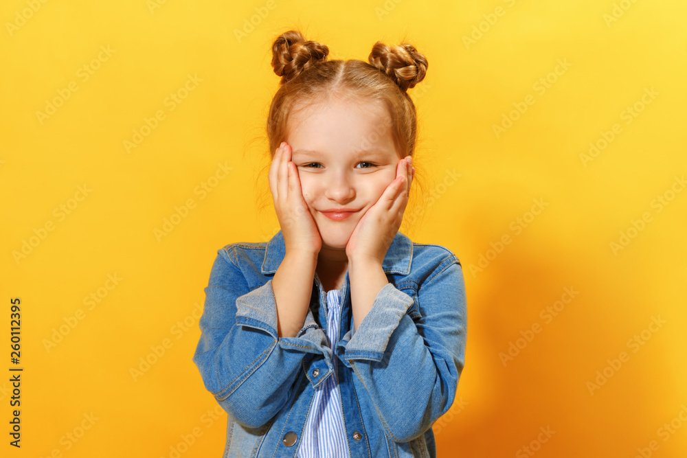 Closeup portrait of a cute attractive little girl on yellow background. Child hands face and looks into the camera. Closeup portrait of a cute attractive little girl on yellow background. Child hands face and looks into the camera.