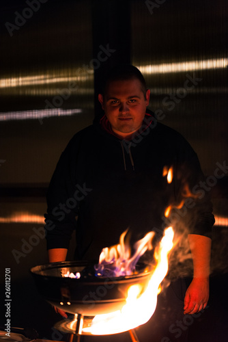 Obraz na plátně White man standing behind charcoal barbecue grill fire showing a pyromaniac face