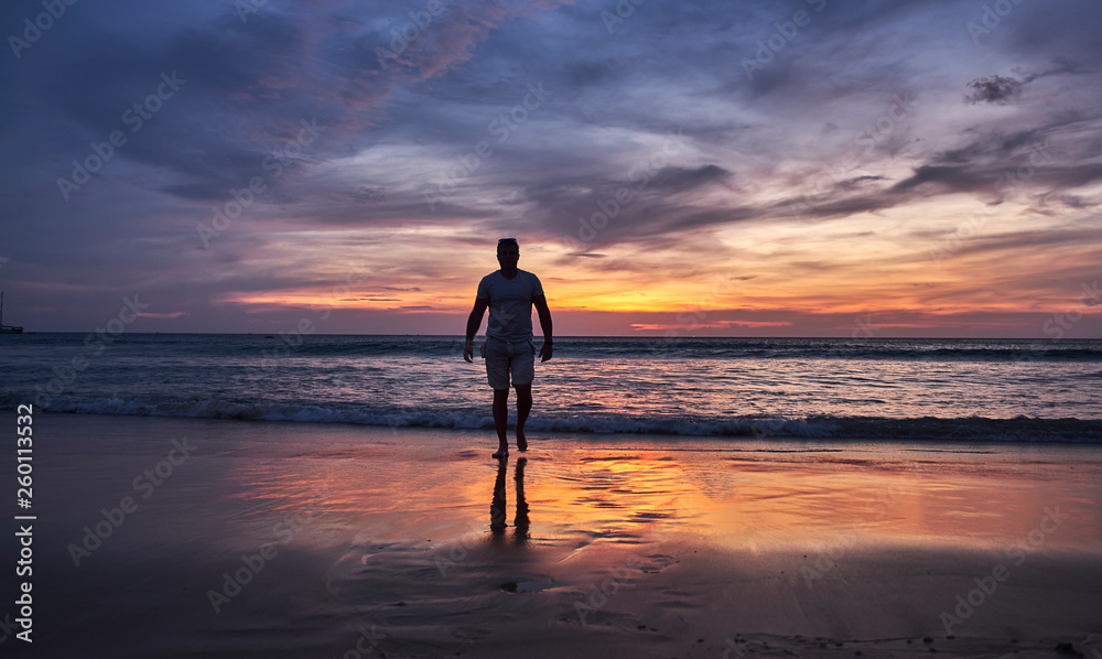 A man walks into the water at sunset