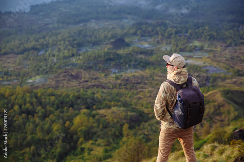 Man tourist looks at the sunrise on the volcano Batur on the island of Blai in Indonesia. Hiker man with backpack travel on top volcano, travel concept