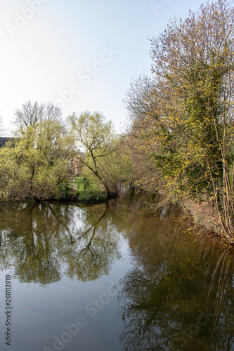 View from the river "Weisse Elster" in Leipzig with trees, bridges and a weir at blue sky