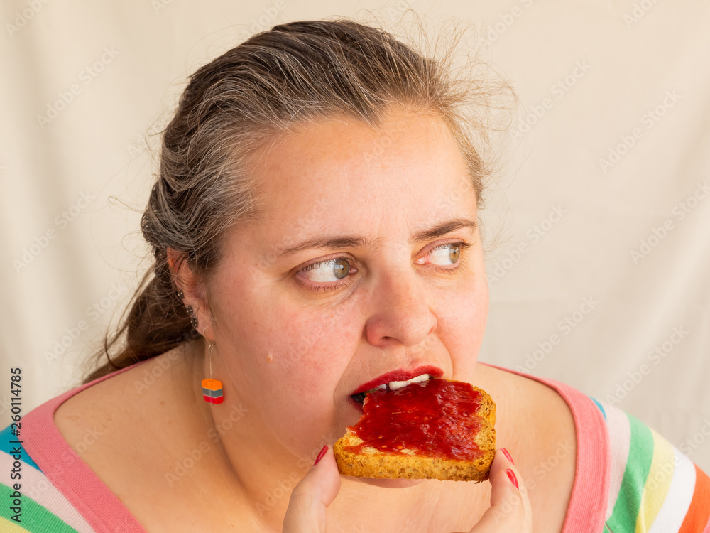An adult woman with red nails and lips eating a rusk with raspberry jam An adult woman with red nails and lips eating a rusk with raspberry jam