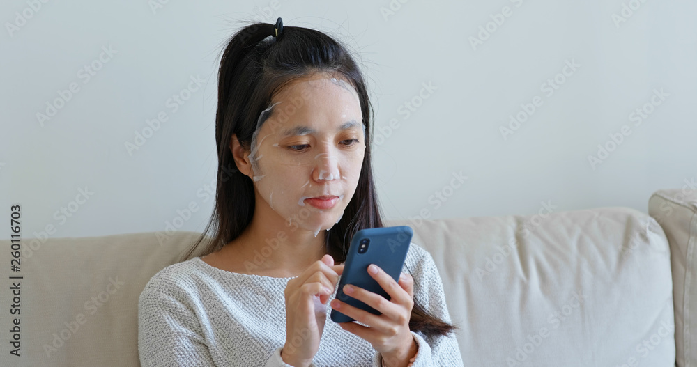 Woman apply paper mask on face at home with use of mobile phone