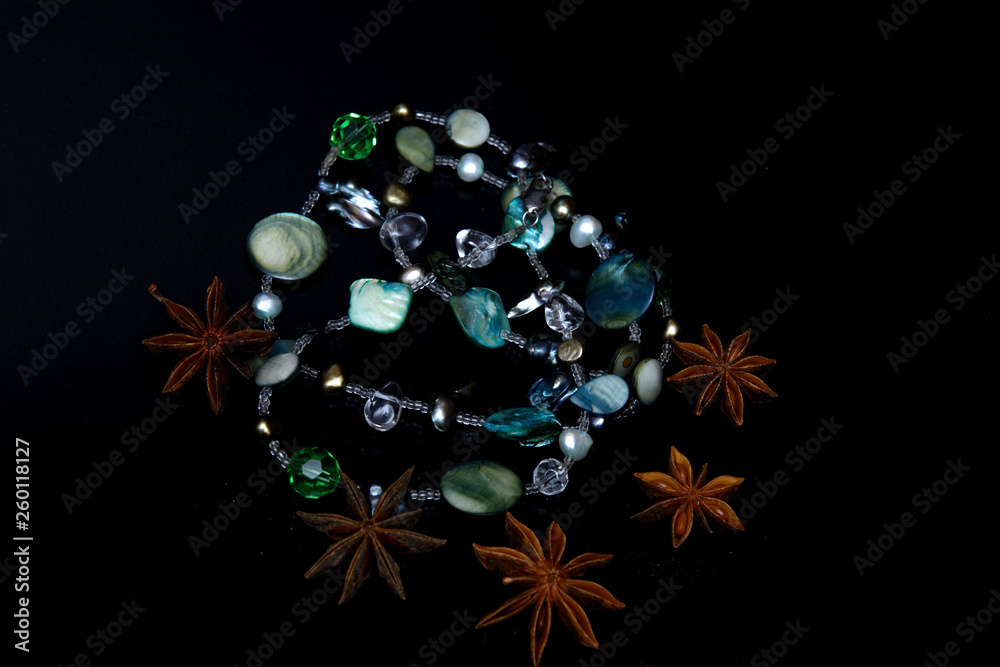 gemstone necklace and star anise on black background