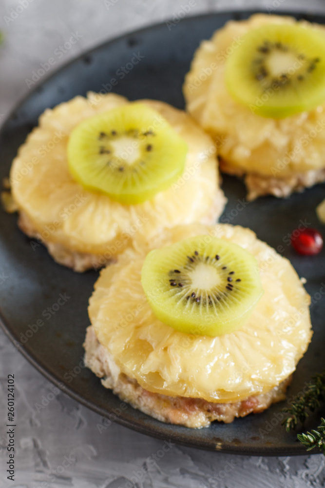 Pieces of baked pork with pineapple, cheese and kiwi on gray background. Pieces of baked pork with pineapple, cheese and kiwi on gray background.