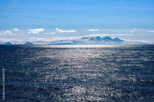 Snow peaks, glaciers and rocks of Aleutian islands in sunny winter day as viewed from ship passing in calm sea photo