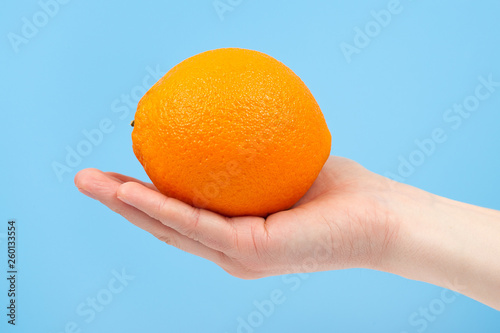 Hand holding organic delicious orange Isolated on blue Background. Healthy eating and dieting concept