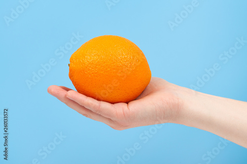 Hand holding organic delicious orange Isolated on blue Background. Healthy eating and dieting concept